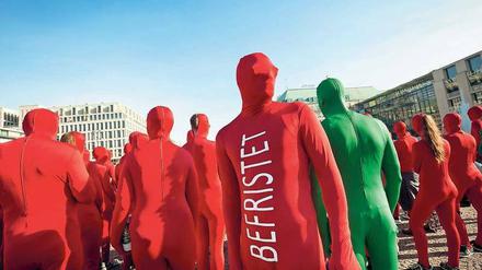 Menschen in roten Ganzkörperanzügen mit der Aufschrift Befristet stehen auf einem Platz.