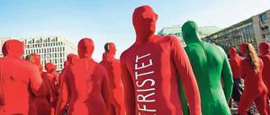 Menschen in roten Ganzkörperanzügen mit der Aufschrift Befristet stehen auf einem Platz.