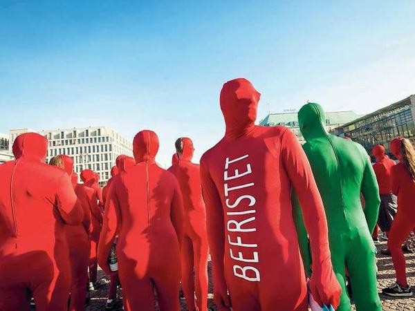 Menschen in roten Ganzkörperanzügen mit der Aufschrift Befristet stehen auf einem Platz.