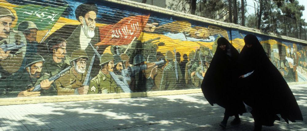 Verschleierte Iranerinnen neben einem Wandgemälde mit dem Konterfei von Ayatollah Khomeini in Teheran, 1984. In dieser Zeit spielt Deborah Ellis' Roman "Wenn der Mond am Himmel steht, denk ich an dich".