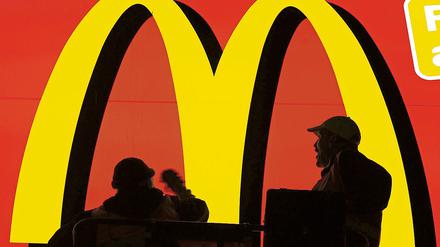Zwei Arbeiter stehen auf einem Hubwagen und reinigen eine große Werbefläche der Fastfood-Filiale McDonald's im Hauptbahnhof in Frankfurt am Main