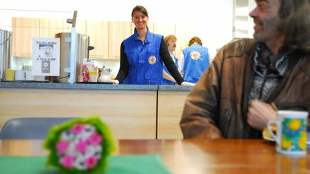 Ein Obdachloser beim Essen in der Bahnhofsmission, im Hintergrund Mitarbeiter der Einrichtung.