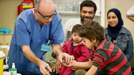 Ein syrischer Flüchtlingsjunge aus Damaskus (Syrien) stempelt im Landesamt für Gesundheit und Soziales (LaGeSo) zusammen mit Arzthelfer Klaus Schmitz seinen Impfausweis. 