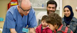 Ein syrischer Flüchtlingsjunge aus Damaskus (Syrien) stempelt im Landesamt für Gesundheit und Soziales (LaGeSo) zusammen mit Arzthelfer Klaus Schmitz seinen Impfausweis.