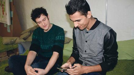 Ein junger Mann hantiert mit einem Smartphone, ein zweiter schaut ihm dabei zu.
