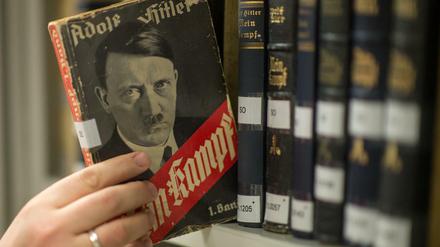 Verschiedene Ausgaben von "Mein Kampf" stehen in einem Bücherregal, eine Hand greift nach einem der Bücher.
