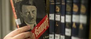 Verschiedene Ausgaben von "Mein Kampf" stehen in einem Bücherregal, eine Hand greift nach einem der Bücher.
