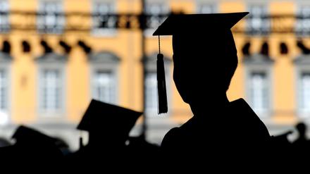 Menschen mit Doktorhüten auf dem Kopf stehen vor einem Universitätsgebäude.