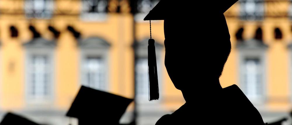 Menschen mit Doktorhüten auf dem Kopf stehen vor einem Universitätsgebäude.