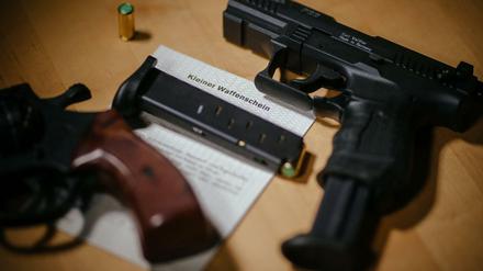 Ein Kleiner Waffenschein zwischen einer Schreckschuss-Pistole, einem Revolver, einem Magazin und einer Knallpatrone. 