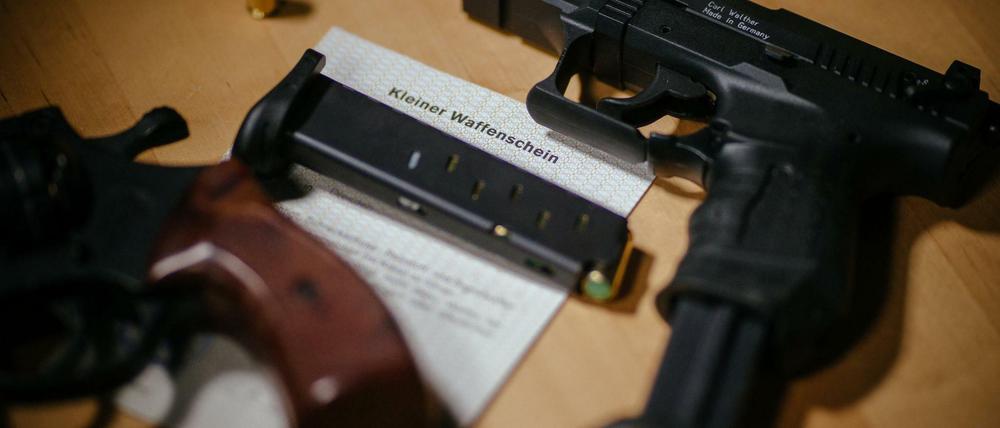 Ein Kleiner Waffenschein zwischen einer Schreckschuss-Pistole, einem Revolver, einem Magazin und einer Knallpatrone.