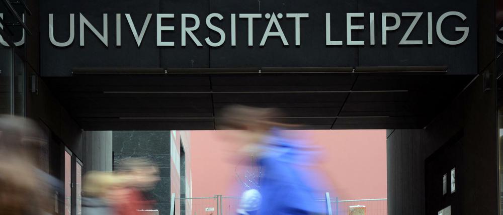 Vor dem Hauptgebäude der Universität Leipzig gehen Passanten, die nur verschwommen zu sehen sind.