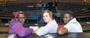 Drei junge Männer sitzen in einem Hörsaal.