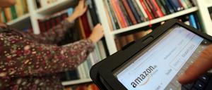 Auf einem Tablet-Computer sucht ein Mann bei dem Online-Versandhaus Amazon nach Literatur, während seine Frau ein Buch aus dem Bücherregal nimmt. 
