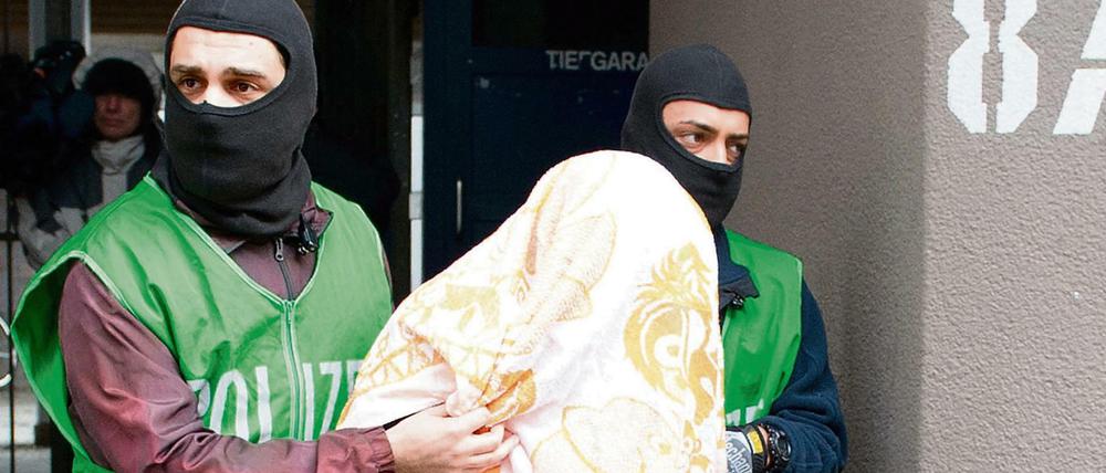 Polizisten führen bei einer Razzia gegen Islamisten am 04.02.2016 in Berlin einen mit einem Tuch verdeckten Verdächtigen ab.