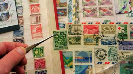 Eine Marke wird mit einer Pinzette aus einem Briefmarkenalbum gezogen.