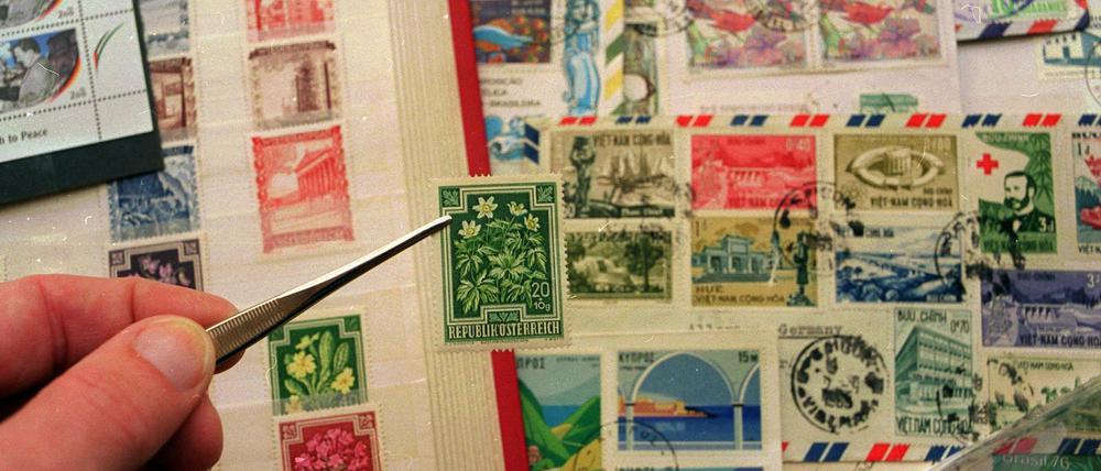 Eine Marke wird mit einer Pinzette aus einem Briefmarkenalbum gezogen.