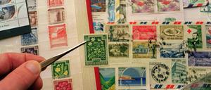 Eine Marke wird mit einer Pinzette aus einem Briefmarkenalbum gezogen.