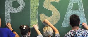 Vier Schüler stehen an einer Tafel und schreiben den Schriftzug "Pisa".