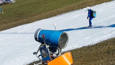 Ein Skifahrer fährt in Garmisch-Partenkirchen (Bayern) am Hausberg auf einem schmalen Kunstschneeteppich an einer Schneekanone vorbei.
