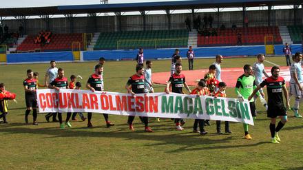 Amedspor-Spieler mit Aufruf. Auf dem Plakat steht: "Lasst Kinder nicht sterben, lasst sie zum Spiel kommen" vor dem Hinspiel im Viertelfinale des türkischen Pokals gegen Fenerbahce. 