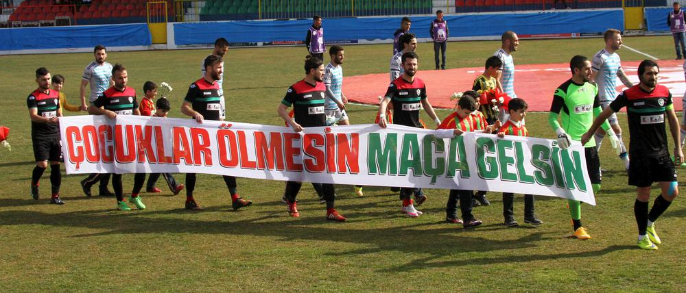Amedspor-Spieler mit Aufruf. Auf dem Plakat steht: "Lasst Kinder nicht sterben, lasst sie zum Spiel kommen" vor dem Hinspiel im Viertelfinale des türkischen Pokals gegen Fenerbahce.