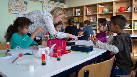 Eine Lehrerin spricht mit Kindern, die in einer Schulklasse an einem Tisch sitzen.