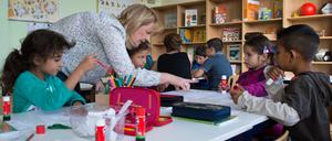Eine Lehrerin spricht mit Kindern, die in einer Schulklasse an einem Tisch sitzen.