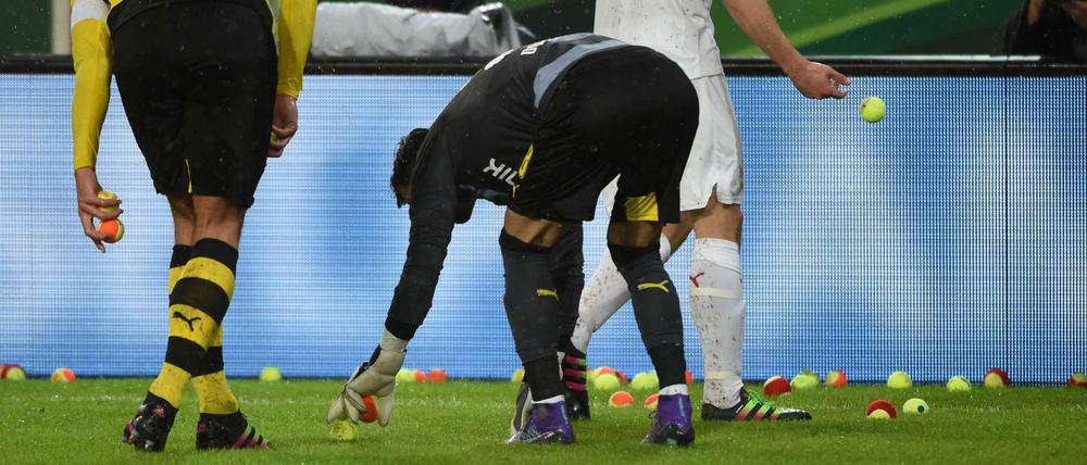 Fußball DFB-Pokal Viertelfinale: VfB Stuttgart - Borussia Dortmund am 09.02.2016 in der Mercedes-Benz-Arena in Stuttgart (Baden-Württemberg). Stuttgarts Christan Gentner (hinten), Dortmunds Mats Hummels (r) und Dortmunder Torwart Roman Bürki sammeln Tennisbälle vom Spielfeld, die von Dortmunder Fans auf den Platz geworfen wurden. Foto: Marijan Murat/dpa (Wichtiger Hinweis: Der DFB untersagt die Verwendung von Sequenzbildern im Internet und in Online-Medien während des Spiels (einschließlich Halbzeit). Sperrfrist! Der DFB erlaubt die Publikation und Weiterverwertung der Bilder auf mobilfunkfähigen Endgeräten (insbesondere MMS) und über DVB-H und DMB erst nach Spielende.) +++(c) dpa - Bildfunk+++