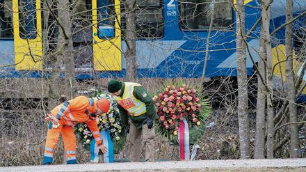 Ein Feuerwehrmann und ein Polizist betrachten Kränze am 10. Februar 2016 vor der Unfallstelle eines Zugunglücks in der Nähe von Bad Aibling.