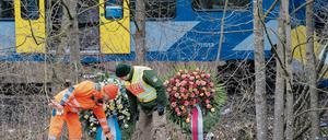 Ein Feuerwehrmann und ein Polizist betrachten Kränze am 10. Februar 2016 vor der Unfallstelle eines Zugunglücks in der Nähe von Bad Aibling.