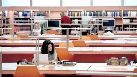 Eine junge Frau sitzt in einer Bibliothek und arbeitet am Laptop.
