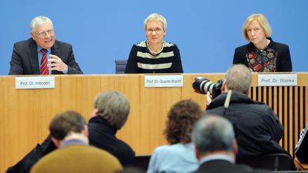 Ein Mann und zwei Frauen sitzen auf einem Podium, der Mann gestikuliert.