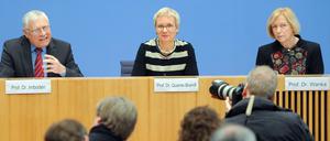 Ein Mann und zwei Frauen sitzen auf einem Podium, der Mann gestikuliert.