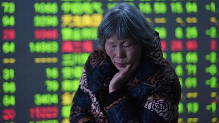 Eine ältere Chinesin steht in Hangzhou in der Provinz Zhejiang vor den aktuellen Börsenkursen. In China sind sinkende Kurse grün gefärbt. 