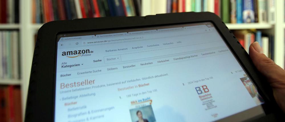  Auf einem Tablet-Computer ist die Seite des Online-Versandhaus Amazon vor einem Bücherregal geöffnet. 