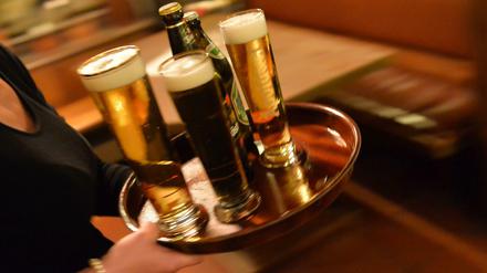Eine Bedienung trägt in einem Lokal ein Tablett mit Bier. 