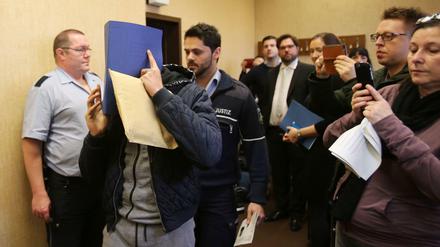 Der Angeklagte kommt am Mittwoch in Köln mit einem Ordner vor dem Gesicht in den Verhandlungssaal. Die ersten Prozesse im Zusammenhang mit der Kölner Silvesternacht sind eröffnet worden. Die Angeklagten stehen wegen Diebstahls vor Gericht.