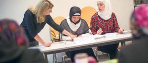 Junge Frauen mit Kopftüchern sitzen an Tischen in einem Klassenzimmer, eine andere Frau erklärt ihnen etwas.