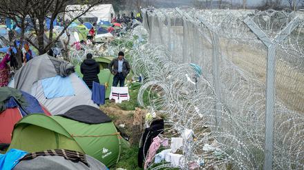 Flüchtlinge stehen am 07.03.2016 im Flüchtlingslager in Idomeni an der Grenze zwischen Griechenland und Mazedonien vor ihren Zelten am mit Stacheldraht gesicherten Grenzzaun. Nur noch wenige Flüchtlinge aus Syrien und dem Irak werden täglich über die Grenze gelassen. Foto: Kay Nietfeld/dpa +++(c) dpa - Bildfunk+++