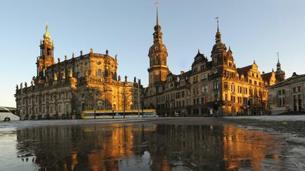 Angestrahlt von der tiefstehenden Abendsonne spiegelt sich das Ensemble des Dresdner Residenzschlosses in einer vereisten Pfütze auf dem Theaterplatz in Dresden. 