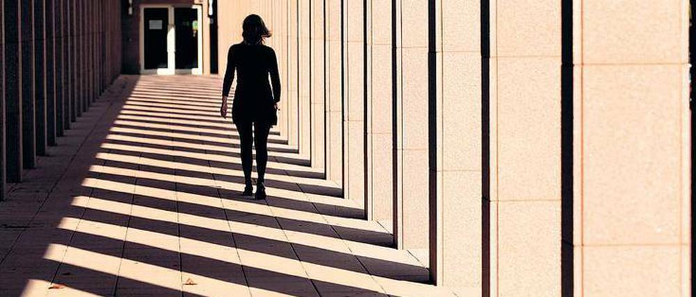 Eine Frau, die an einem Gebäude entlang geht, ist von hinten als Silhouette zu sehen.