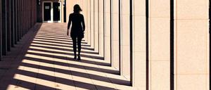 Eine Frau, die an einem Gebäude entlang geht, ist von hinten als Silhouette zu sehen.