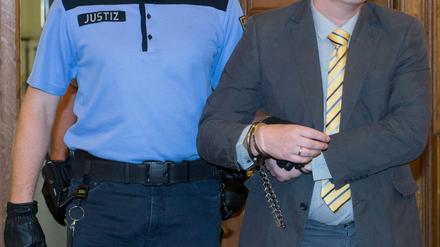 Der Angeklagte Sebastian T. (r) wird am 20.08.2015 vor Prozessbeginn im Landgericht in Leipzig von einem Justizbeamten mit Handschellen in den Saal geführt. Der Angeklagte soll einen 22-jährigen Bekannten im Jahr 2013 an einen Fahrstuhl in der 14. Etage eines Wohnhauses in Leipzig gelockt und diesen in den Schacht gestoßen haben.