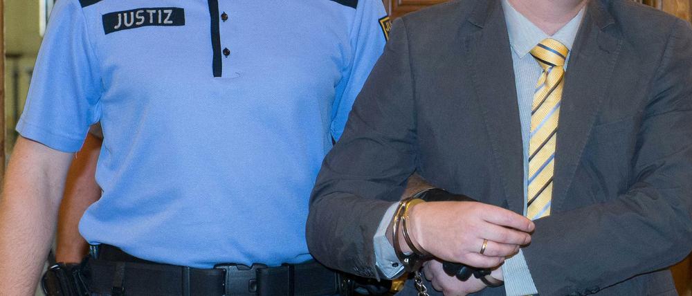 Der Angeklagte Sebastian T. (r) wird am 20.08.2015 vor Prozessbeginn im Landgericht in Leipzig von einem Justizbeamten mit Handschellen in den Saal geführt. Der Angeklagte soll einen 22-jährigen Bekannten im Jahr 2013 an einen Fahrstuhl in der 14. Etage eines Wohnhauses in Leipzig gelockt und diesen in den Schacht gestoßen haben.