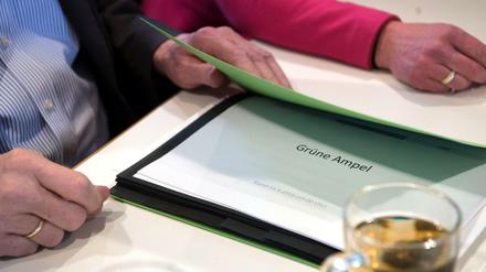 Der baden-württembergische Ministerpräsident Winfried Kretschmann hat im Haus der Architekten in Stuttgart (Baden-Württemberg) eine Mappe in der Hand, in der ein Dokument mit der Aufschrift "Grüne Ampel" liegt. 