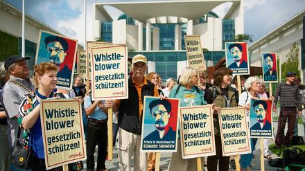 Menschen stehen vor dem Bundeskanzleramt und halten Schilder hoch, auf denen politisches Asyl für Edward Snowden gefordert wird.
