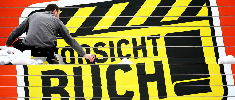 Ein Werbetechniker klebt das Logo "Vorsicht Buch!" der Leipziger Buchmesse auf eine Treppe in der Glashalle der Leipziger Messe. 