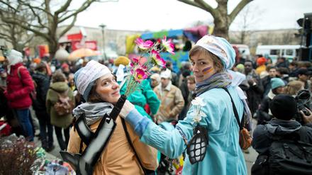 Mit Waffenattrappen, in denen Blumen stecken, nehmen zwei Frauen am "Karneval der Geflüchteten" teil. 