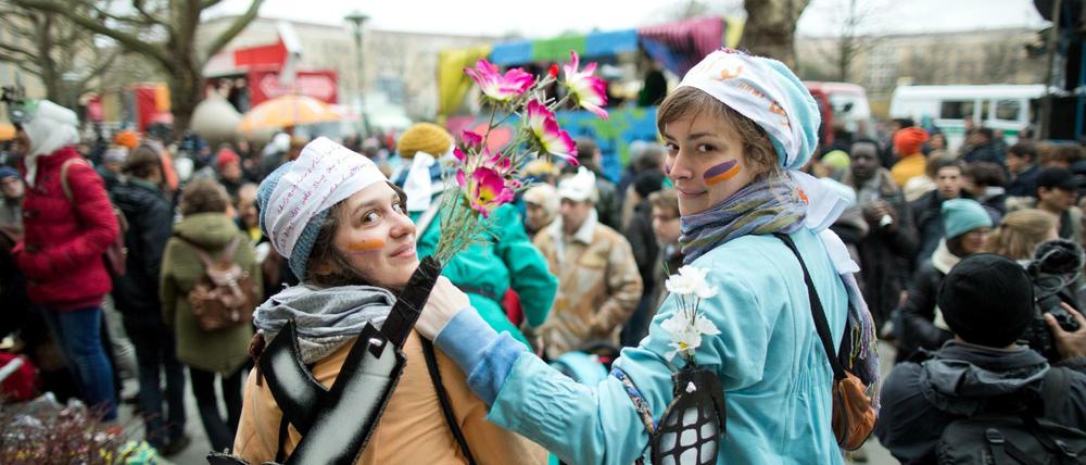 Mit Waffenattrappen, in denen Blumen stecken, nehmen zwei Frauen am "Karneval der Geflüchteten" teil.
